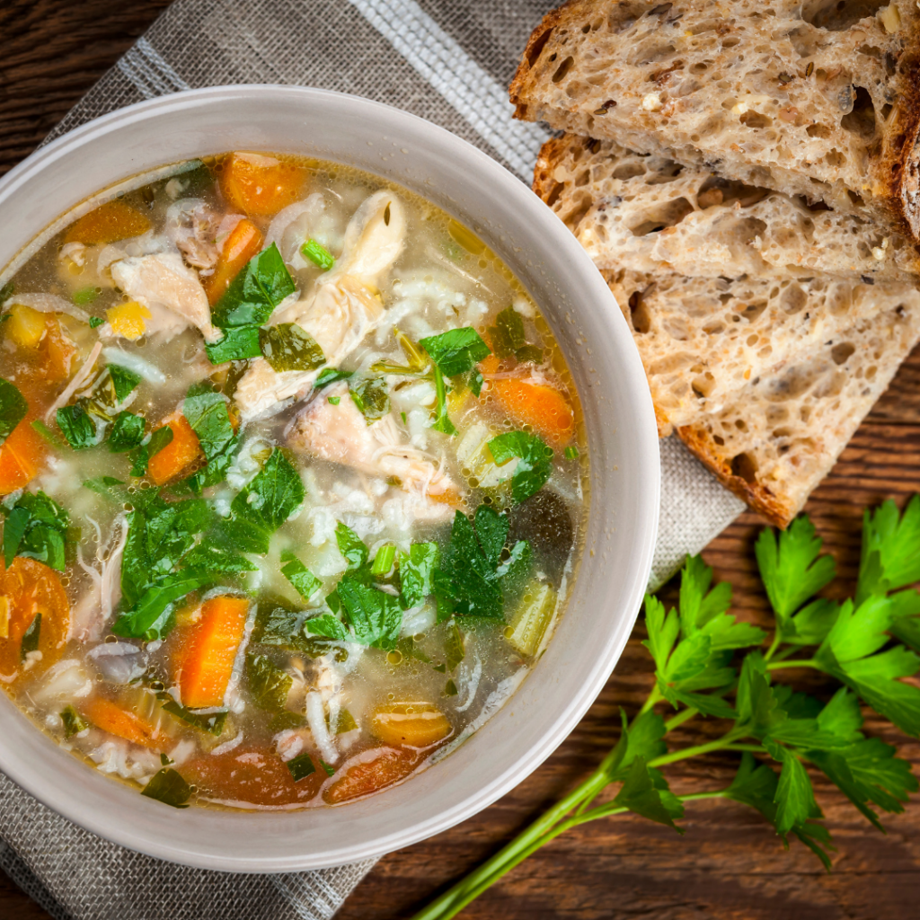 A bowl of chicken soup with bread on the side.